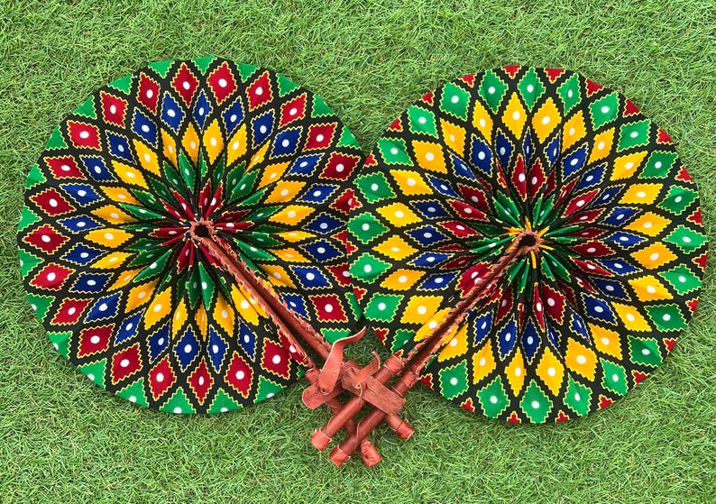 Pode incluir: Dois leques de m&atilde;o coloridos com fundo preto e um padr&atilde;o geom&eacute;trico de diamantes verdes, amarelos, vermelhos, azuis e brancos e pontos brancos. Os leques est&atilde;o dobrados e t&ecirc;m cabos de madeira.