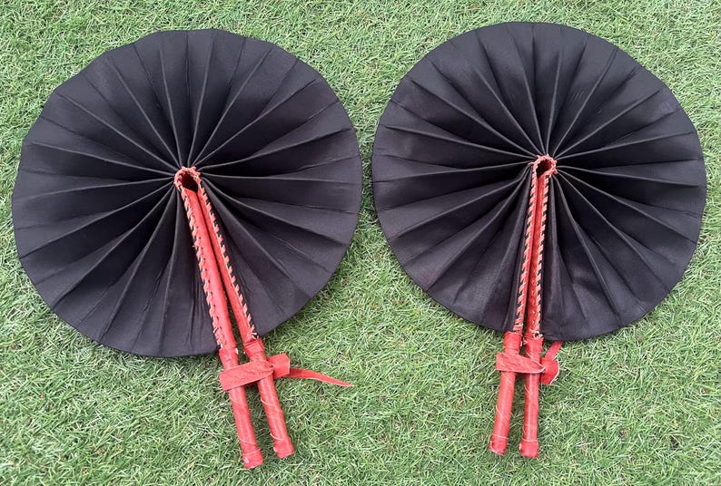 May include: Two black folding fans with red wooden handles. The fans are closed and have a pleated design.