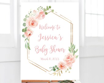 May include: A white welcome sign with a gold geometric frame and pink floral accents. The text reads "Welcome to Jessica's Baby Shower March 10, 20XX".