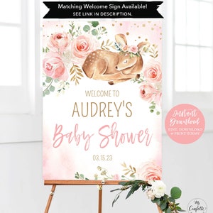 May include: A pink and gold baby shower welcome sign with a floral design and a sleeping fawn with a floral crown. The sign says "Welcome to Audrey's Baby Shower 03.15.23".
