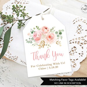 May include: A white gift tag with a floral design and the words "Thank You" in pink script. The tag also includes the text "For Celebrating With Us! Chloe 5.18.20". The tag is tied with twine and rests on a gift wrapped in brown paper.