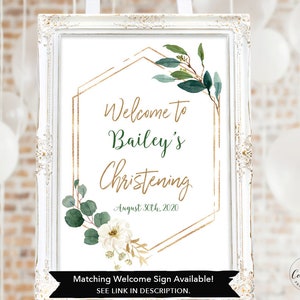 May include: A white framed sign with gold geometric shapes and green foliage. The text on the sign reads "Welcome to Bailey's Christening August 30th, 2020". The sign also includes the text "Matching Welcome Sign Available! SEE LINK IN DESCRIPTION."
