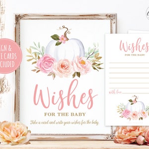May include: A printable sign for a baby shower with a white pumpkin and pink flowers. The sign says "Wishes for the Baby" and includes instructions to take a card and write wishes for the baby. The sign is framed in a rustic white frame.