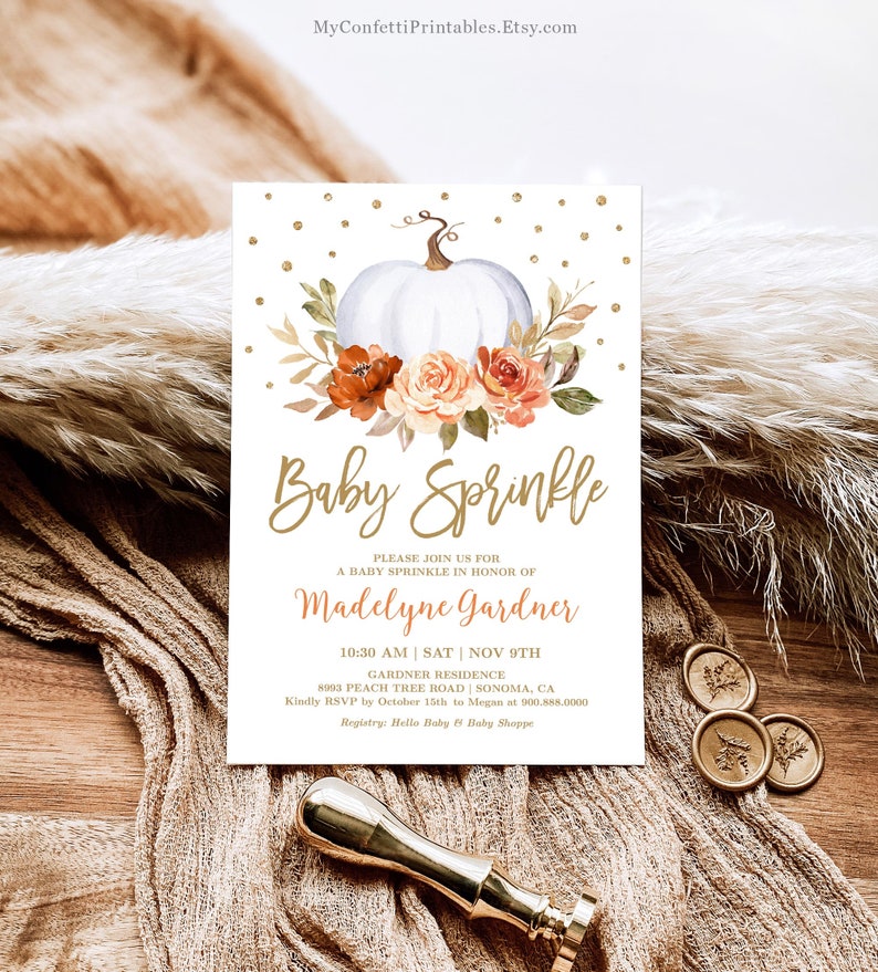 May include: A white pumpkin with orange and peach flowers and greenery. The text "Baby Sprinkle" is written in gold script. The text "Please join us for a baby sprinkle in honor of Madelyne Gardner" is written in gold. The date and time of the event are listed as "10:30 AM | SAT | NOV 9TH". The location is listed as "Gardner Residence 8993 Peach Tree Road Sonoma, CA". The RSVP information is listed as "Kindly RSVP by October 15th to Megan at 900.888.0000". The registry information is listed as "Registry: Hello Baby & Baby Shoppe".