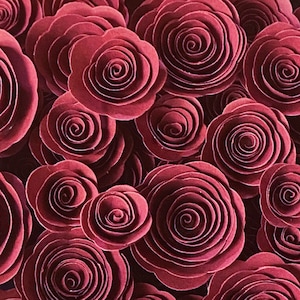 May include: A close-up of a collection of burgundy paper roses. The roses are arranged in a cluster, with the center of each rose being a spiral of paper.