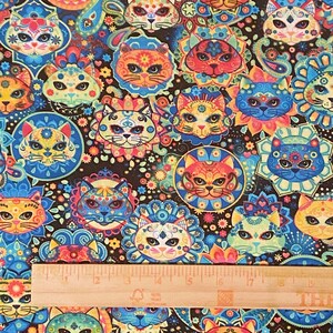 May include: A colorful fabric with a repeating pattern of sugar skull cats. The cats are wearing flowers and have intricate designs. The background is black with a paisley pattern.
