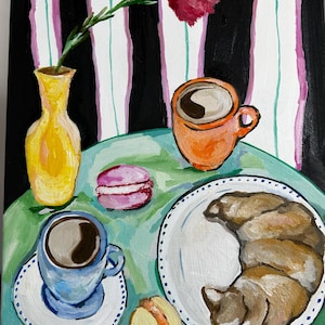 May include: An original painting of a breakfast scene. A yellow vase holds a red flower. A blue cup of coffee sits on a saucer, next to a plate with a croissant. There is also an orange cup of coffee and two macaroons.
