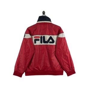 May include: Red and white FILA jacket with a navy blue collar. The jacket features the FILA logo in white and navy blue across the back. The jacket has a ribbed hem and cuffs.