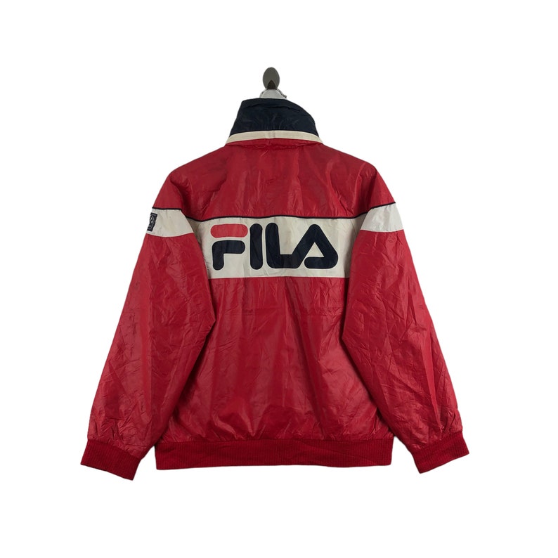 May include: Red and white FILA jacket with a navy blue collar. The jacket features the FILA logo in white and navy blue across the back. The jacket has a ribbed hem and cuffs.