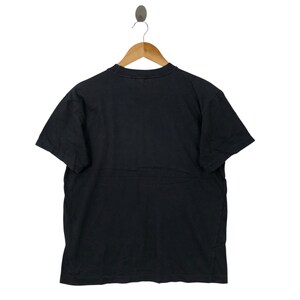 May include: A black short-sleeved t-shirt hanging on a wooden hanger. The shirt is made of a soft material and has a crew neck. The background is white.