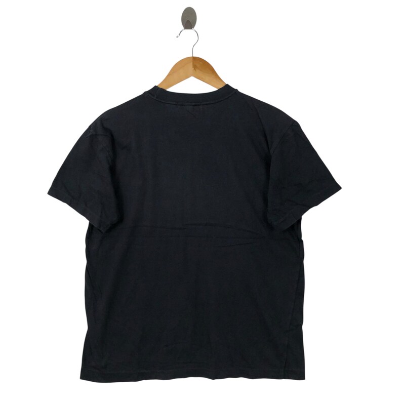 May include: A black short-sleeved t-shirt hanging on a wooden hanger. The shirt is made of a soft material and has a crew neck. The background is white.