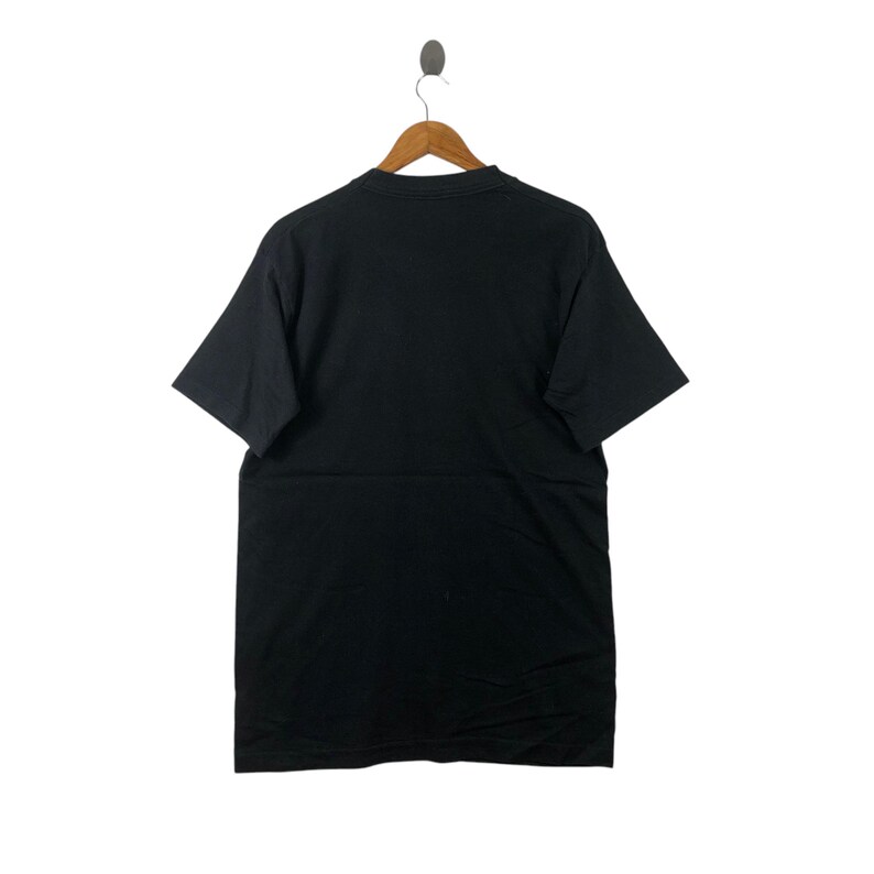 May include: A black short-sleeved t-shirt hanging on a wooden hanger. The t-shirt is plain with no visible graphics or text.