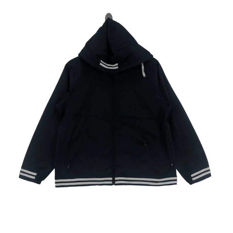 K&ouml;nnte beinhalten: Eine schwarze Kapuzenjacke mit wei&szlig;en Streifen am Saum und einem wei&szlig;en Streifen an der Kapuze. Die Jacke hat einen Rei&szlig;verschluss und zwei Taschen.