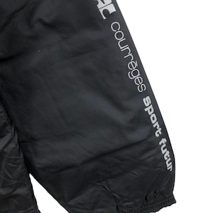 May include: Black athletic jacket with the text "courr&egrave;ges sport futur" printed in silver on the sleeve. The jacket appears to be made of a lightweight, possibly water-resistant material.