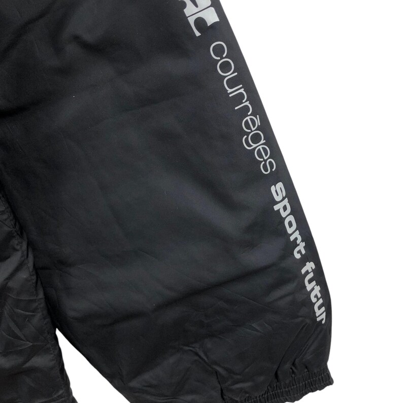 May include: Black athletic jacket with the text "courr&egrave;ges sport futur" printed in silver on the sleeve. The jacket appears to be made of a lightweight, possibly water-resistant material.