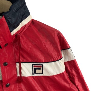 May include: Red and white vintage jacket with a navy blue collar. The jacket features a white stripe across the chest and a logo patch. The jacket has a drawstring and button closures. A retro style windbreaker.