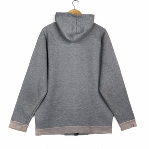 以下が含まれることがあります： ジッパー留めと裾と袖にライトグレーのトリムが付いたグレーのフード付きスウェットシャツです。