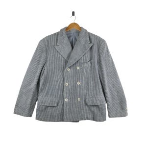 Pode incluir: Um blazer cinza de dupla abotoadura listrado com quatro botões. O blazer tem lapela de entalhe e dois bolsos.