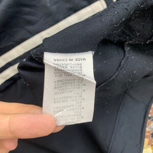 K&ouml;nnte beinhalten: Ein schwarzes und wei&szlig;es Pflegeetikett mit japanischem Text, der "MADE IN CHINA" lautet, und Anweisungen zum Waschen und Trocknen des Kleidungsst&uuml;cks.