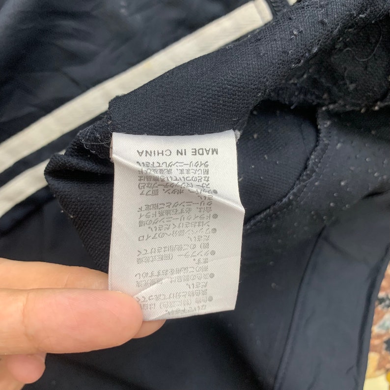 K&ouml;nnte beinhalten: Ein schwarzes und wei&szlig;es Pflegeetikett mit japanischem Text, der "MADE IN CHINA" lautet, und Anweisungen zum Waschen und Trocknen des Kleidungsst&uuml;cks.