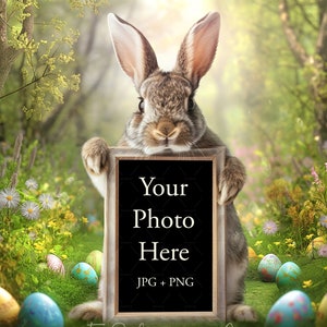 Könnte beinhalten: Ein braunes und graues Kaninchen hält ein gerahmtes Tafelschild mit dem Text "Your Photo Here JPG + PNG" in einer üppigen grünen Wiese mit bunten Ostereiern. Der Hintergrund zeigt eine verschwommene Waldszene mit Sonnenlicht.