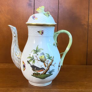 May include: White porcelain coffee pot with a lid, featuring a bird and floral design. The pot has a gold rim and handle, with a decorative spout. The lid is topped with a yellow flower and butterfly accents.