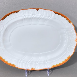 Könnte beinhalten: Eine weiße ovale Servierplatte mit einem erhabenen, geprägten Design und einem goldenen und orangenen Rand.