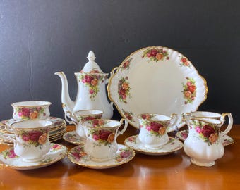 May include: A vintage tea set with a cream-colored teapot, sugar bowl, creamer, and six teacups and saucers. The set features a floral pattern with red, pink, and yellow roses. The set is made of fine bone china and has a gold trim.