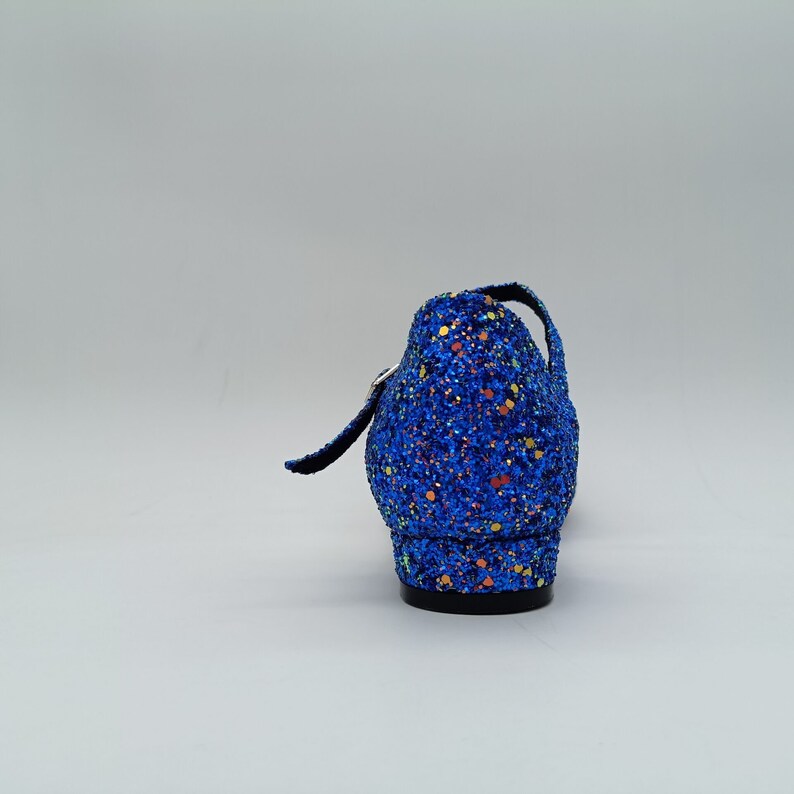 May include: A blue glitter shoe with a black heel and a strap. The shoe has a sparkly finish with small colourful dots.