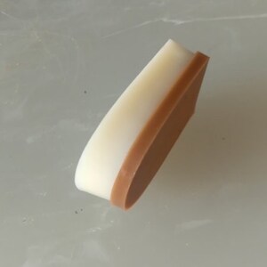 May include: A close-up of a 1.5 cm high heel for a shoe. The heel is made of two layers of material, a white top layer and a brown bottom layer.