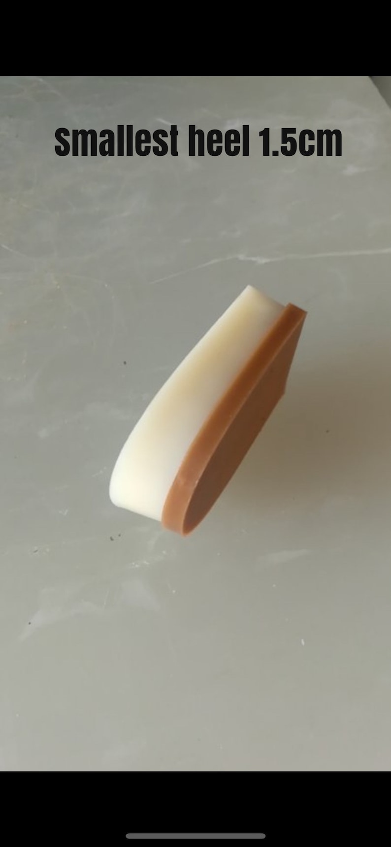 May include: A close-up of a 1.5 cm high heel for a shoe. The heel is made of two layers of material, a white top layer and a brown bottom layer.