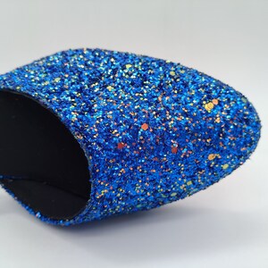 May include: A close-up of a blue glitter slipper with a black lining. The glitter is iridescent and has a variety of colours, including blue, green, and gold.