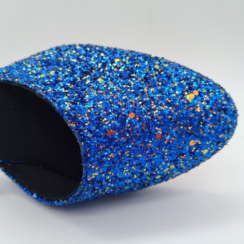 May include: A close-up of a blue glitter slipper with a black lining. The glitter is iridescent and has a variety of colours, including blue, green, and gold.