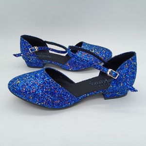 May include: A pair of blue glitter heeled shoes with ankle straps and buckles. The shoes have a black sole and are labelled "emily jane - designs".