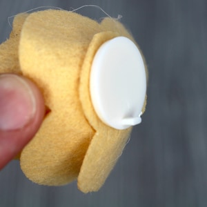 May include: A yellow felt flower with a white adhesive backing. The flower has five petals and is attached to the backing with a small white tab.