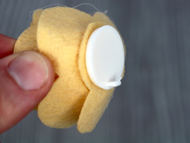 May include: A yellow felt flower with a white adhesive backing. The flower has five petals and is attached to the backing with a small white tab.