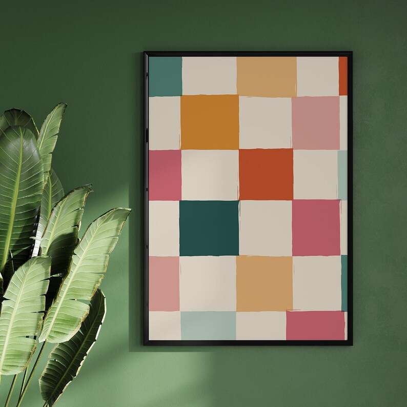 K&ouml;nnte beinhalten: Ein gerahmter Kunstdruck mit einem abstrakten Muster aus farbigen Quadraten. Die Quadrate sind in den Farbt&ouml;nen T&uuml;rkis, Orange, Rosa, Rot und Creme gehalten. Das Kunstwerk wird vor einer dunkelgr&uuml;nen Wand mit einer gro&szlig;en Pflanze im Vordergrund ausgestellt.