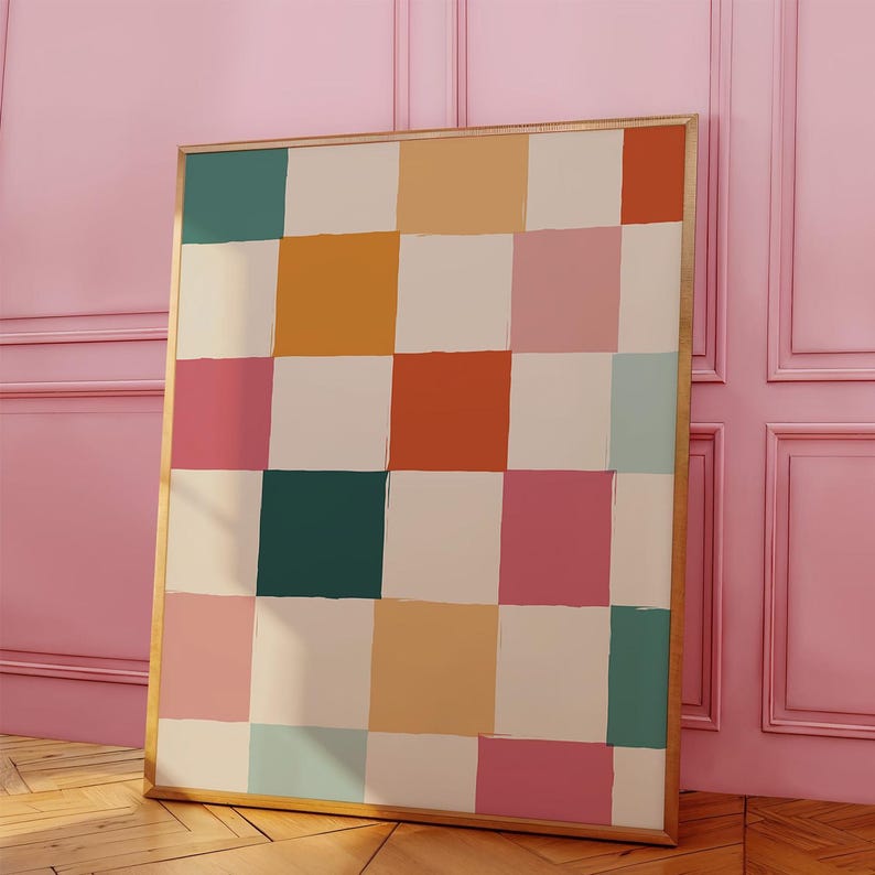 K&ouml;nnte beinhalten: Ein gerahmtes Kunstwerk mit einem Raster aus farbigen Quadraten in T&uuml;rkis, Orange, Rosa und Creme. Das Kunstwerk hat einen goldenen Rahmen und lehnt an einer rosa Wand. Das abstrakte Design erinnert an ein Schachbrettmuster.