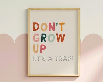 May include: A framed print with the text "DON'T GROW UP (IT'S A TRAP)" in colorful, playful lettering. The background is a light beige color.