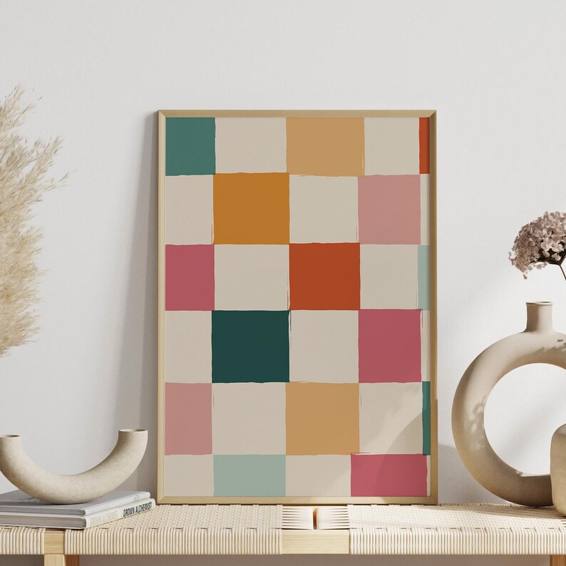 K&ouml;nnte beinhalten: Ein gerahmter Kunstdruck mit einem abstrakten Muster aus farbigen Quadraten. Die Quadrate sind in T&uuml;rkis-, Orange-, Rosa- und Cremet&ouml;nen gehalten, mit einem beigen Hintergrund. Das Kunstwerk wird auf einer Holzbank mit dekorativen Vasen ausgestellt.