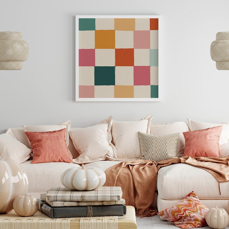 K&ouml;nnte beinhalten: Ein gerahmtes Kunstwerk mit einem Schachbrettmuster in T&uuml;rkis-, Orange-, Rosa- und Beiget&ouml;nen h&auml;ngt &uuml;ber einem cremefarbenen Sofa. Dekorative Kissen und K&uuml;rbisse tragen zur gem&uuml;tlichen Wohnzimmeratmosph&auml;re bei.