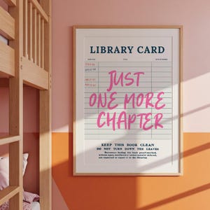 May include: Framed print with a library card design. The text reads "Just One More Chapter" in pink script. The print includes a section for dates and a reminder to keep the book clean.