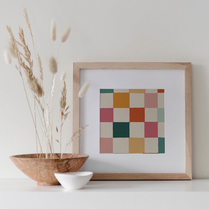 K&ouml;nnte beinhalten: Ein gerahmter Druck mit einem farbenfrohen Schachbrettmuster in Rosa, Orange, Gr&uuml;n und Gelb. Das Kunstwerk wird in einem hellen Holzrahmen mit wei&szlig;em Passepartout pr&auml;sentiert. Eine Holzschale und eine kleine wei&szlig;e Schale befinden sich im Vordergrund.