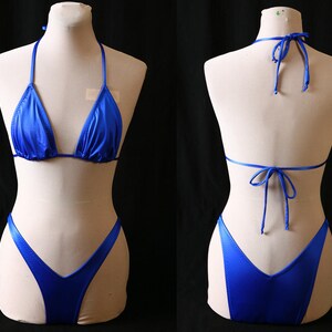 May include: A two-piece, royal blue bikini set. The top is a triangle style with halter ties, and the bottoms are a classic cut. The shiny fabric reflects light, creating a vibrant appearance. The bikini is displayed on a mannequin.