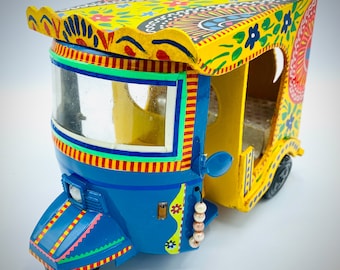 May include: A miniature three-wheeled vehicle model painted in bright blue and yellow with intricate floral patterns. The roof features a scalloped edge, and the side is adorned with a string of small, round, light-colored beads. The number 9 is visible.