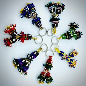 May include: Seven colorful beaded keychains with bells. Each keychain features a tassel-like design with multiple strands of beads in various colors, including red, blue, green, yellow, and black.