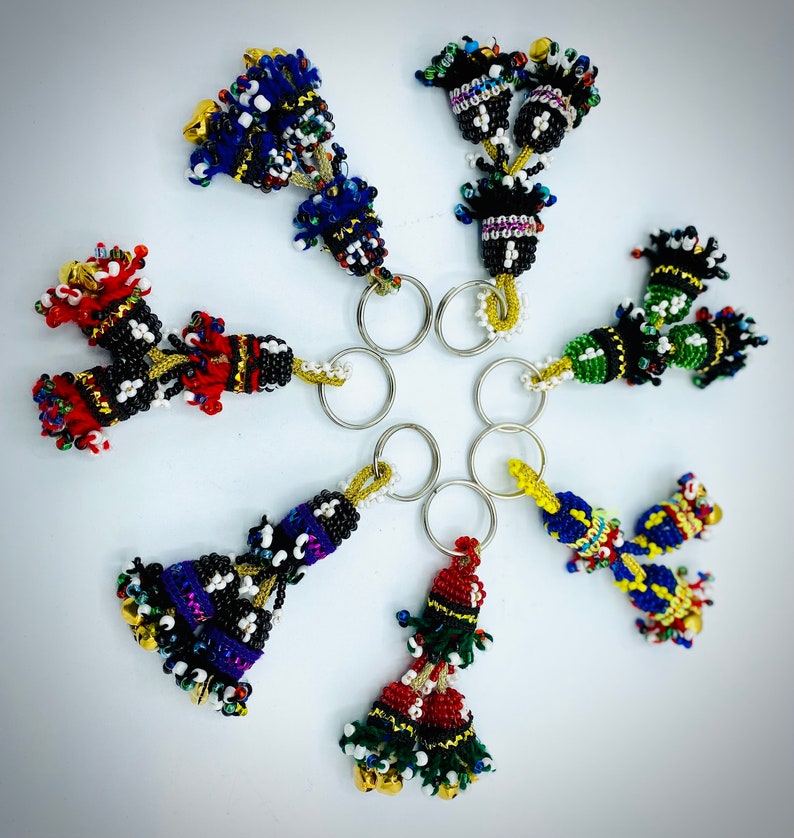 May include: Seven colorful beaded keychains with bells. Each keychain features a tassel-like design with multiple strands of beads in various colors, including red, blue, green, yellow, and black.