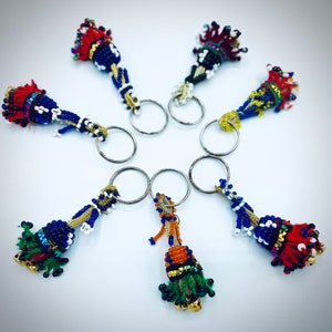 May include: Seven colorful beaded keychains with tassels hanging from silver key rings. The keychains are made of blue, red, green, yellow, and white beads.