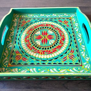 May include: A teal wooden serving tray with a hand-painted design. The design features a circular pattern with red, yellow, white, and black accents.