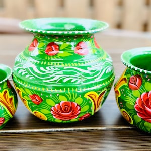 以下が含まれることがあります： 花柄が描かれた緑色の陶器製の鉢が3つあります。鉢は赤、黄、白の絵の具で装飾されています。一番大きな鉢は他の2つの鉢よりも背が高いです。